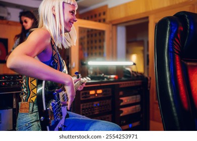 Profile view of a professional female guitarist playing bass guitar at music recording studio. Smiling female musician sitting at music recording studio with bass guitar and playing it and recording. - Powered by Shutterstock