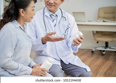 Profile View Of Senior Asian Patient Listening To Her Doctor With Interest While He Giving Her Instructions How To Take Pills Correctly, Interior Of Modern Office On Background