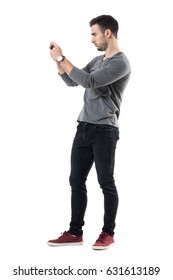 Profile View Of Serious Young Casual Man Holding Cellphone Taking Photo. Full Body Length Portrait Isolated Over White Studio Background.