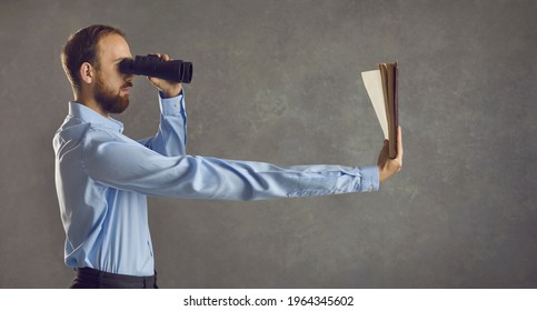 Profile view of serious young guy who needs glasses looking in binoculars and reading book he's holding in long extended arm. Humorous concept of dealing with presbyopia, bad eyesight, vision problems - Shutterstock ID 1964345602