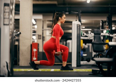 Profile view of a strong woman doing lunges with dumbbells in a gym. - Powered by Shutterstock