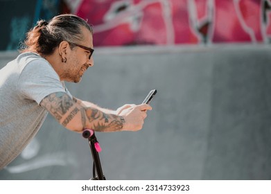 Profile view of an urban middle-aged man with tattoos sitting on his bmx bike and taking a break from riding in a skate park while smiling at the phone. A cool older man is smiling at the phone. - Powered by Shutterstock