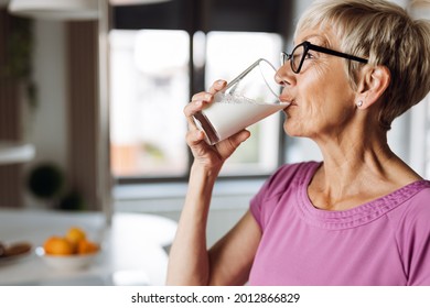 Profile view of a woman drinking fresh milk from a glass in the kitchen