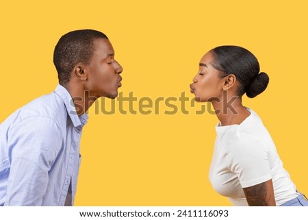 Profile view of young black couple puckering up for kiss, their lips almost touching, set against bright yellow background, illustrating intimacy