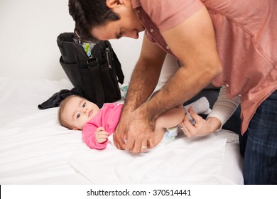 Profile View Of A Young Couple Changing A Diaper And Clothing Of Their Baby Daughter At Home