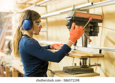 Profile view of a young female carpenter using a drill press on a wood board in a woodshop - Powered by Shutterstock