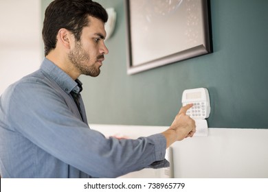 Profile view of a young Hispanic man using a keypad to arm his home alarm system before leaving