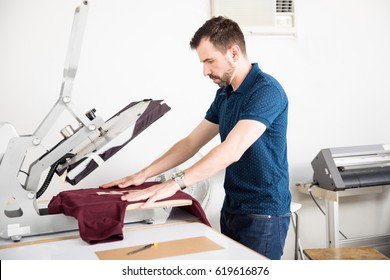 Profile view of a young man setting up a shirt on a serigraph press before printing - Powered by Shutterstock