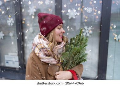 profile view of a young modern girl in winter clothes with fir branches in her hands on the background of a Christmas showcase.Holiday concept.New Year celebration