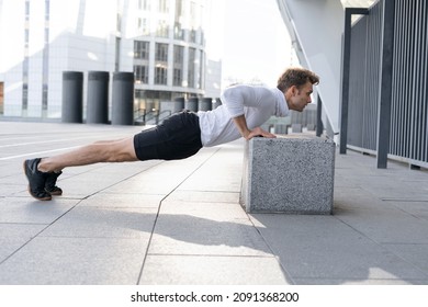 Profile View Of Young Sportsman On Sport Training Outdoors Doing Push Or Press Ups Exercise, Standing In Low Plank Position. Concentrated Man Warm Up His Body Before Daily Workout, Full Length
