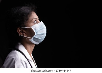 Profile View Of Young Woman Doctor With Opened Eyes In Medical Mask On Black Background Looking Up - Concept Of Hope And Fight To End Coronavirus Or Covid-19 Crisis.