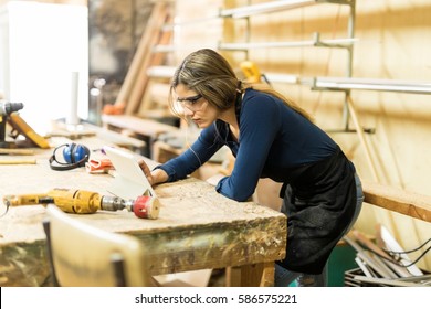 Profile View Of A Young Woman Looking At A Tablet Computer While Working In A Woodshop