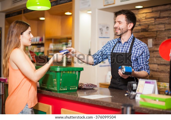 Profile view of a young woman paying with a\
credit card to a store clerk in a\
supermarket