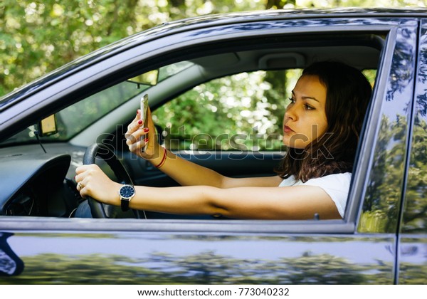 Profile of a woman driver sitting\
on the front seat and making faces while looking in the\
phone.