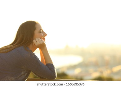 Profile of a woman with eyes closed relaxing at sunset in a balcony 