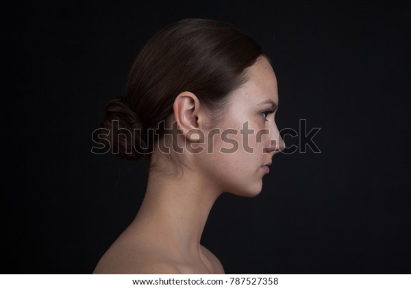 Profile of a woman\'s face without makeup on a\
black background.