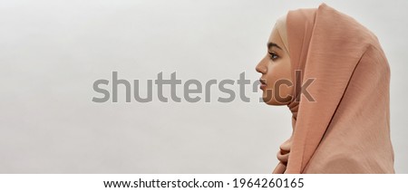 Profile of young arabian girl in traditional hijab posing sideways on white background with copy space, panorama. Beautiful muslim lady