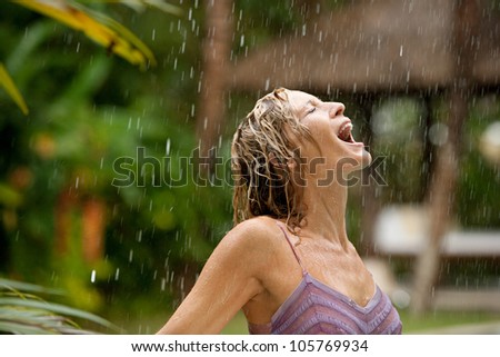 Profile of a young attractive woman under tropical rain with her mouth open.