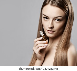 Profile of young beautiful woman with long silky straight hair holding bottle with moistirizing oil for hair rehabilitation or treatment over grey background, copy space. Haircare, beauty, wellness