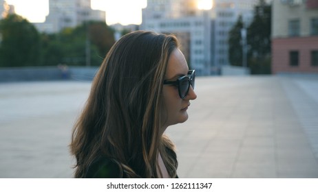 Profile Of Young Business Woman In Sunglasses Walking In City Street. Attractive Businesswoman Commuting To Work With Sun Flare At Background. Confident Girl Being On His Way To Job. Close Up Slow Mo.