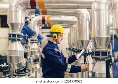 Profile of young Caucasian worker tightening the valve and using tablet while standing in heating plant.