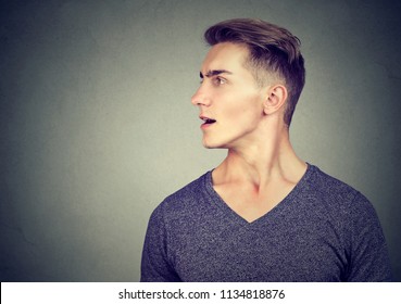 Profile Of Young Handsome Man In Casual Outfit Talking With Mouth Opened Looking Away On Gray Background