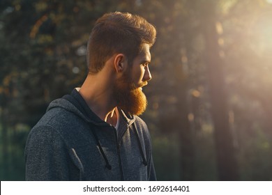 Profile young handsome serious bearded man. Hipster walking in a park. Portrait of man looking at sunrise in the forest Copy free space for advertising