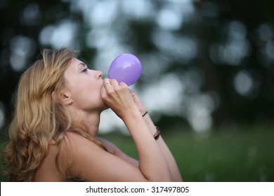 Profile of a young woman blowing up a purple balloon outdoors 