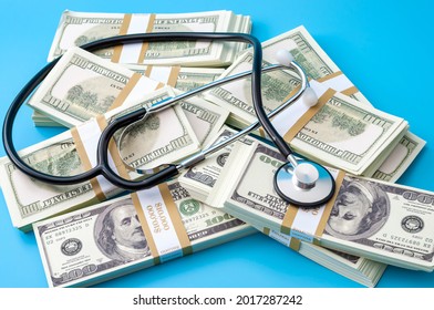 Profit Driven Hospital, Premium Medical Insurance Payment And High Doctor Bills Expense Concept With Stethoscope, Stacks Of Dollars And No People Isolated On Blue Background