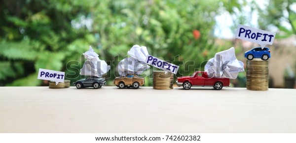 Profit\
growth concept, rolls of gold coin increasing and miniature cars\
truck carry crumpled paper and blue vehicle with \