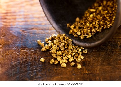 Profit, trade and exchange. Gold nuggets spilling out from a grungy old metal container, placed on a old wooden table.Shallow depth of field.