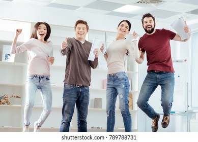 Profitable contract. Jolly gay  four colleagues laughing  while celebrating  good deal and jumping