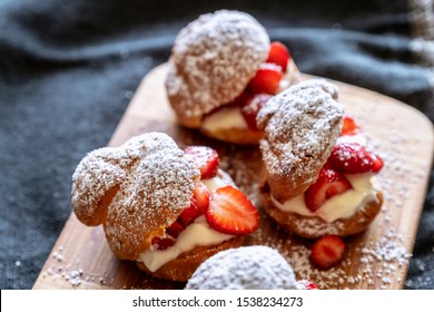Profiteroles sprinkled with powdered sugar, filled with cream cheese cream and cream and sliced strawberries on top. Dark background. Classic dessert