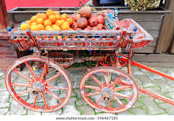 Profusely ornate red painted wooden cart\
containing oranges and pomegranates on the seafront promenade to\
the Soustheast of the ancient city of Side-East Pamphylian\
coast-Antalya\
province-Turkey.