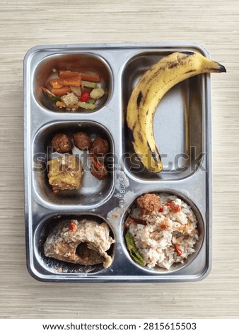 Program Makanan Bergizi Gratis MBG untuk siswa di Indonesia. Menu lengkap dalam nampan stainless 5 sekat berisi nasi putih, ikan kuah, bakso, tahu goreng, tumis sayur wortel jagung muda, dan buah pisang.
