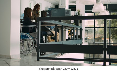 Programer with chronic disability typing source code on computer, working with cloud computing terminal window. Software engineer in wheelchair writing ai algorithm in it company office. Tripod shot.