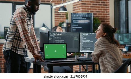 Programer Working At Desk With Multiple Computer Screens And Laptop With Green Screen Chroma Key Mockup Running Code. Software Developer Compiling Source Algorithm Interrupted By Colleague.