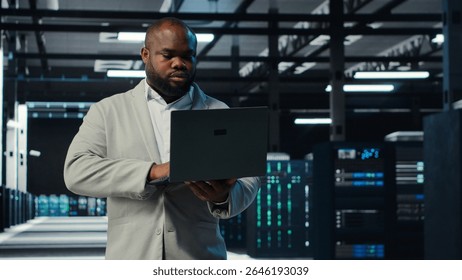 Programmer in data center using laptop, testing equipment failover scenarios. Server farm IT professional uses software on notebook, ensuring data accessibility, camera B