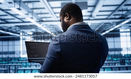 Programmer doing yearly maintenance checkup using laptop to prolong data center electronics life span. IT professional in server farm monitoring server infrastructure using notebook, camera B