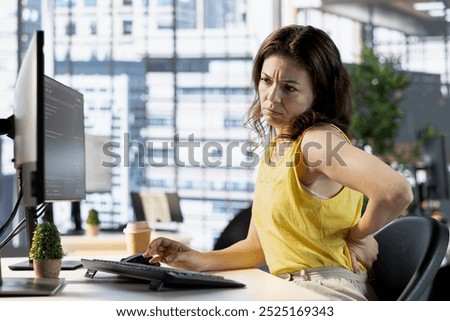 Programmer feeling back pain while sitting at desk testing company software to minimize occurrence of bugs. Fatigued woman suffering pain from incorrect posture while writing code