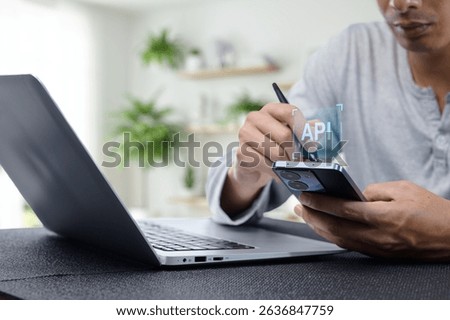 A programmer focuses on API development with a laptop and smartphone in a modern workspace, showcasing the integration of technology and innovative solutions.