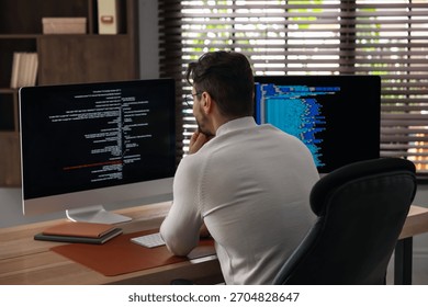 Programmer in glasses working on computer with dual monitors at table in office
