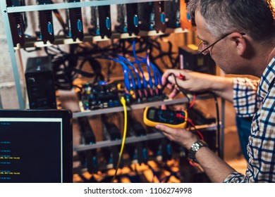 Programmer holding a wattmeter measuring cryptocurrency mining rig electrical energy consumption.  - Shutterstock ID 1106274998