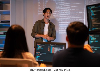 Programmer presenting software project to team in modern office.Asian software developers working on multiple screens displaying Source code and application diagrams at night.coding technologies.