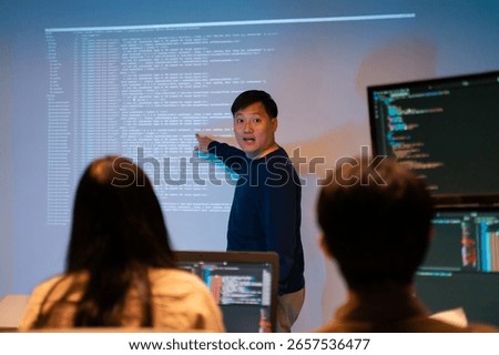 Programmer presenting software project to team in modern office.Asian software developers working on multiple screens displaying Source code and application diagrams at night.coding technologies.