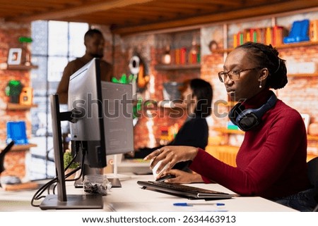 Programmer in startup office using large language model to get help with coding project. African american worker interacting with AI LLM chatbot PC GPT software on PC in software development workplace