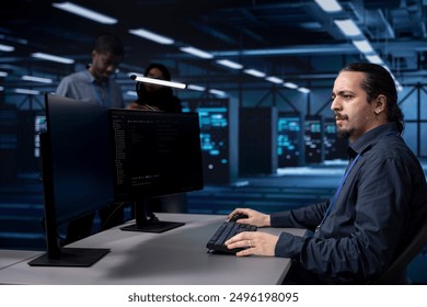 Programmer typing on PC in data center, updating systems to protect servers from exploitable software vulnerabilities. IT expert coding and looking for errors causing equipment to slow down