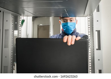 Programmer In Virus Protection Tools Works In The Server Room Datacenter. Maintenance Of Computer Equipment Under Quarantine.A Guy In Medical Mask Is Working In Front Of A Laptop.