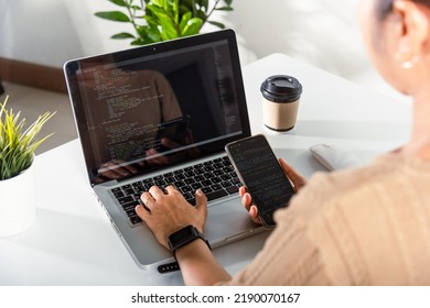 Programmer woman looking mobile phone program code at workplace, software developer hands typing data coding programming javascript with laptop computer, IT startup concept, Web application design