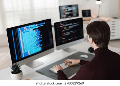 Programmer working on computer with dual monitors at white table in office